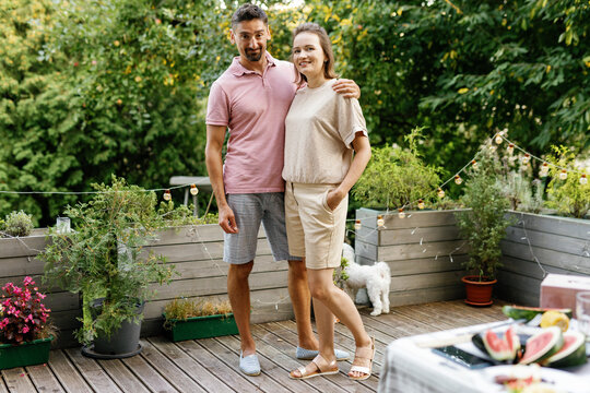 Front view of pleased couple hugging and looking at camera on terrace