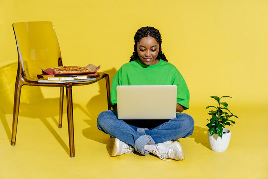 Woman working on laptop while sitting on floor with pizza nearby