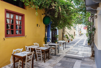 Inviting outdoor tables line a picturesque alley in Nafplio, Greece, where colorful buildings and greenery create a serene atmosphere perfect for leisurely meals.
