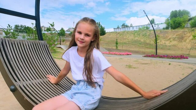 Child plays on wooden swing. Child swing, kid girl smile. Child girl happiness dream entertainment. Happy little girl swings on swing in park. Family walk