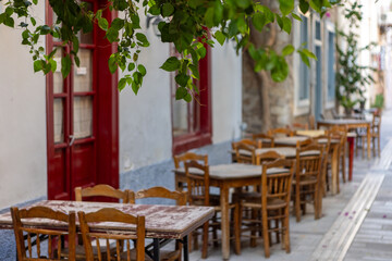 Rustic wooden tables and chairs create an inviting atmosphere in Nafplio, Greece, inviting visitors to relax and savor local delicacies in this picturesque setting.