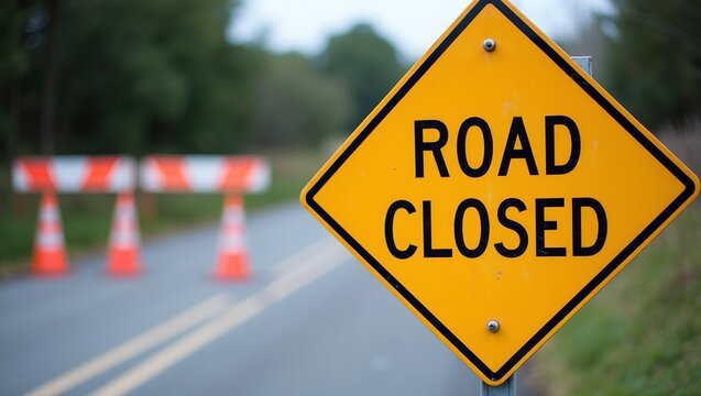Yellow Road Closed sign on metal barrier with roadblock and detour cones