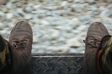 Person's worn boots resting on a train platform with gravel below