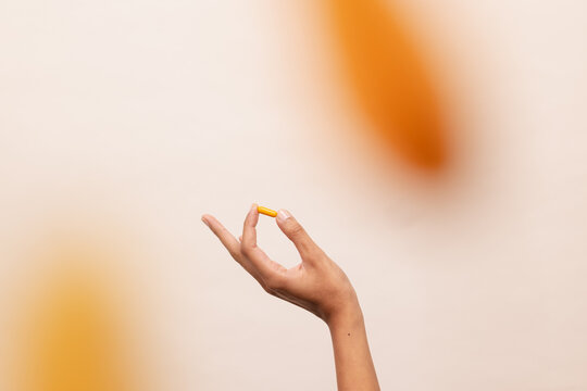 Hand Holding Yellow Capsule Against Soft Background