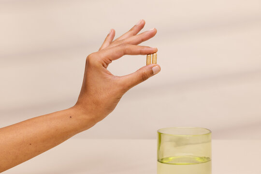 Hand Holding Two Pills Over Glass of Water 