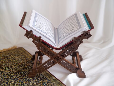 A photo of an open Quran placed on an ornate wooden stand, known as a "rihal."
