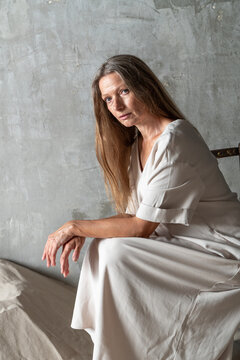 Thoughtful woman sitting on a chair against a concrete wall.