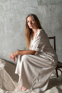 Woman in light dress sitting on a chair in a minimalist setting.