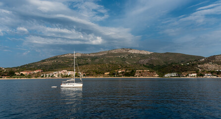 Fototapeta premium Sailboat sailing on a vast blue sea on a sunny day with cloudy sky near shore of Greek island