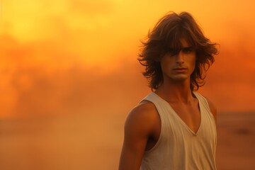 Fototapeta premium A man with long hair stands in front of a sunset