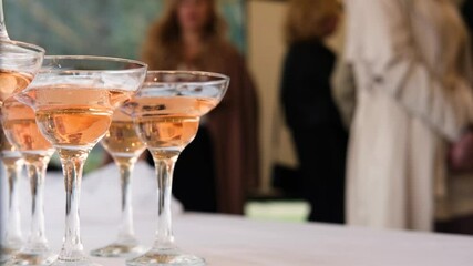 A slender young woman approaches a pyramid of glasses with pink champagne
