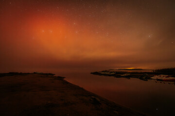 A calm, misty riverbank at night, with boats resting along the shore. Warm orange and yellow lights...