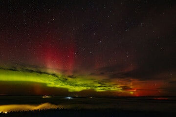 A vivid aurora borealis with striking red and green hues lights up the starry night sky above a...