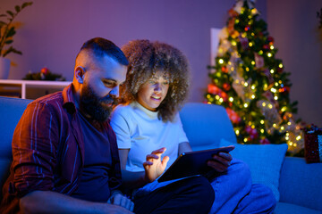Young couple browsing internet on tablet next to christmas tree