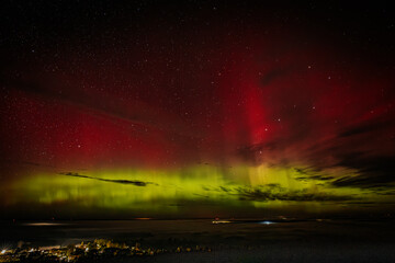 A vivid aurora borealis with striking red and green hues lights up the starry night sky above a...