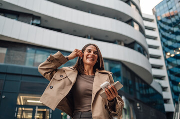 Happy businesswoman listening music walking outside office building