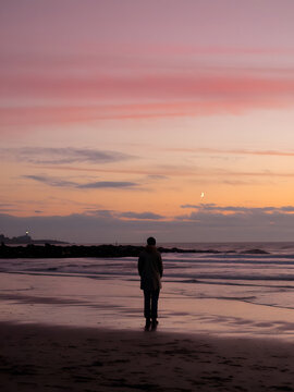 Una persona solitaria parada en una playa por la noche mirando el horizonte contemplando la luna
