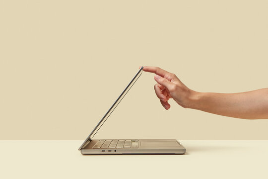 Person pushing down display of laptop standing on light surface