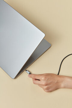 Hand holding black micro usb cable next to plug of pc