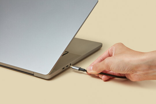 Cropped hand reaching to portable computer with black usb cable