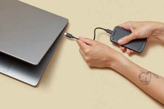 Person connecting external portable drive to laptop with cable