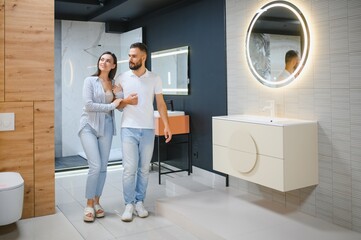 Young couple choosing new bathroom furniture at the plumbing shop with lots of sanitary goods