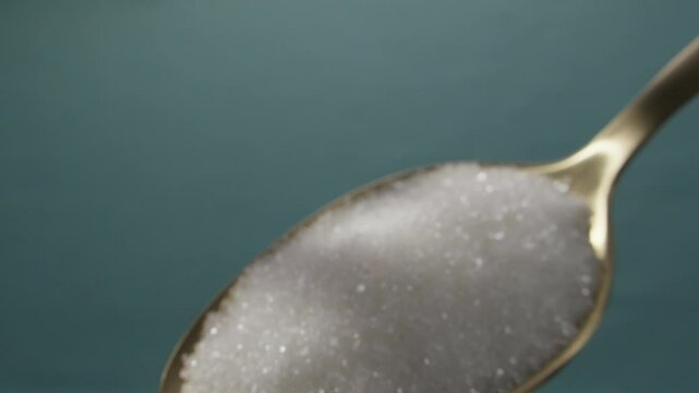 Close-up shot of white granulated sugar in a golden spoon.