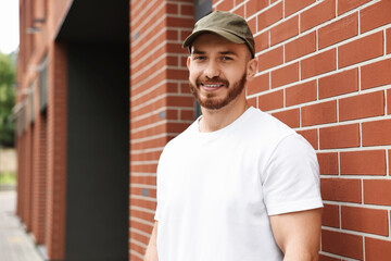 Portrait of smiling man in baseball cap near building outdoors. Space for text