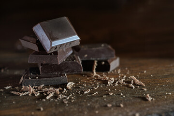 Pieces of organic dark chocolate with a high cocoa content and little sugar stacked on brown rustic wooden planks, a slightly healthy sweet treat with antioxidant flavonoids, copy space
