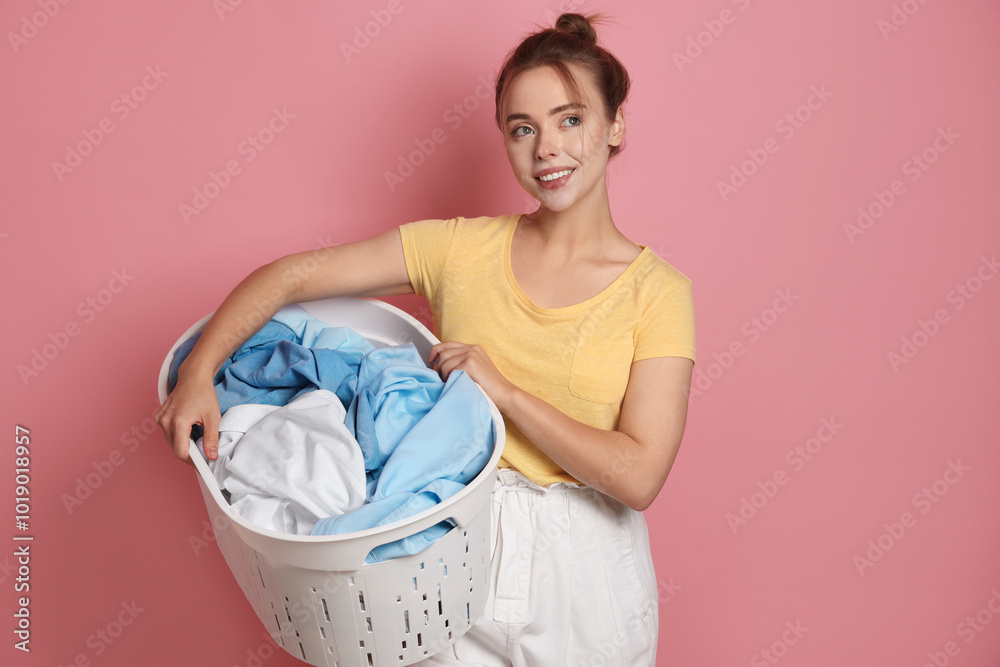 Sticker Happy young housewife with basket full of laundry on pale pink background