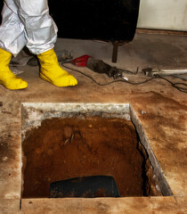 Worker in protective gear next to cut in concrete floor exposes soil over underground oil tank about to be decommissioned. This is part of a controlled, hazardous material removal process.