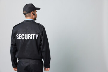 Security guard in uniform with earpiece on grey background, back view. Space for text