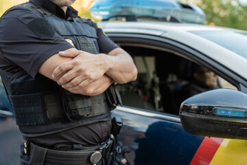 Police officer standing with arms crossed by patrol car