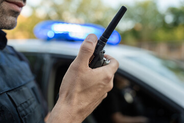 Police officer using walkie talkie near patrol car with flashing lights © Jorge