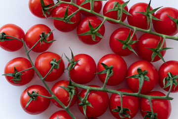 Branches of ripe red cherry tomatoes on a white background. Organic backdrop. Close-up of cherry tomatoes arranged on a white background.