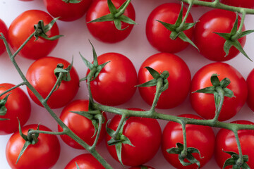Background of cherry tomato branches lying on a white surface. Focus on bright, fresh vegetables. A snack suitable for vegetarian and vegan diets, a product straight from the farm.