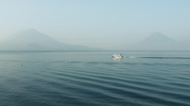 Boats traveling across lake atitlan with volcanos in the background 