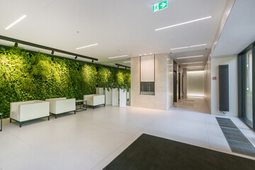 Amazing design of an office hall in a modern building. The wall is decorated with green .plants. White tables and armchairs.