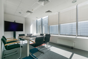 A room for business meetings and negotiations in a modern office. Large TV in the interior. Panoramic window with blinds.