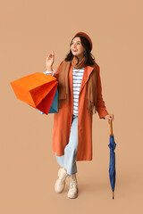 Young woman with shopping bags and umbrella on brown background