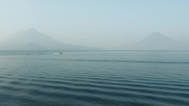 Boats traveling across lake atitlan with volcanos in the background 