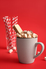 Cup of hot cocoa with marshmallows and waffle on red background