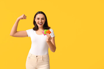 Beautiful young woman with condoms showing muscles on yellow background. Safe sex concept