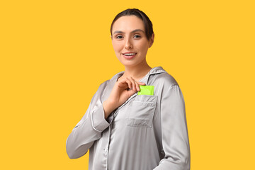 Beautiful young woman putting condom into pocket on yellow background. Safe sex concept