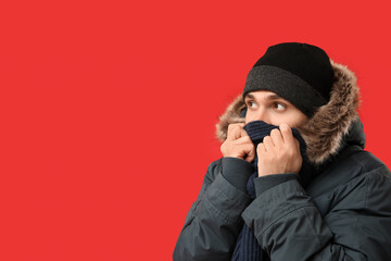 Young man in stylish puffer jacket and scarf on red background