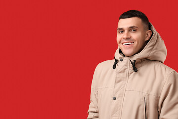 Happy young man in stylish puffer jacket on red background
