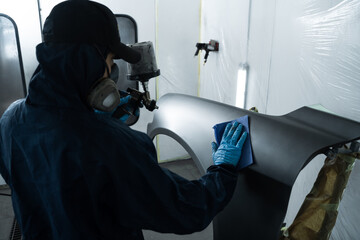 Car painter is changing the color of vehicle using sponge and paint sprayer. Worker is painting car...