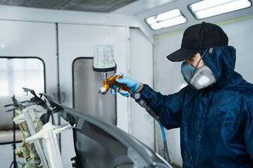 Car painter is finishing his paintwork on vehicle by applying lacquer with paint sprayer. Using...