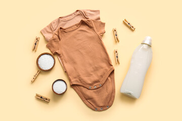 Laundry detergents with clothespins and baby bodysuits on beige background