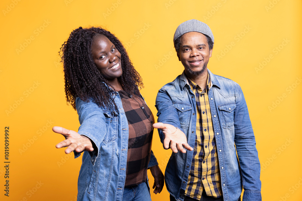 Wall mural smiling african american soulmates pointing at the camera, standing against yellow background and po